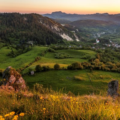 Eine Berglandschaft mit Wiesen und Wäldern bei Roșia Montană in Rumänien ist in orangefarbenes Abendlicht getaucht.