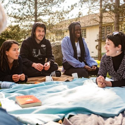Vier junge Menschen sitzen beim kulturweit-Alumnitreffen 2022 im Freien auf einer Decke.